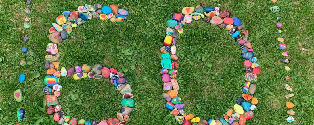 Das Bild zeigt angemalte Steine, die zu der Zahl 60 arrangiert wurden. 