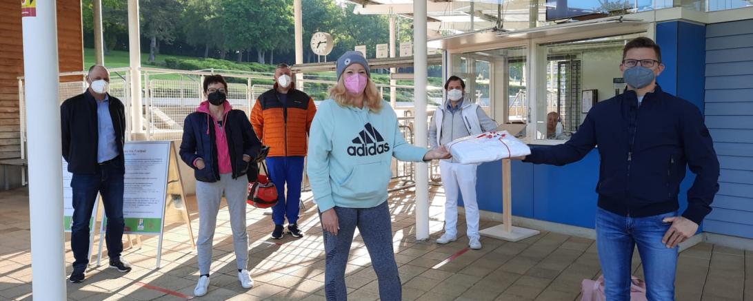 Der Bürgermeister überreicht der ersten Besucherin ein Handtuch. Im Hintergrund sind vier weitere Badegäste zu sehen.