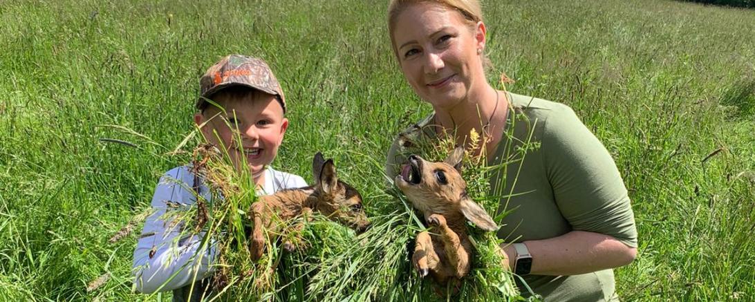 Ein Junge und eine Frau halten zwei Rehkitze in den Händen. 