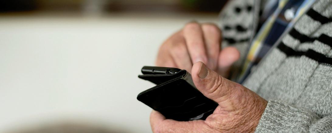 Das Bild zeigt einen älteren Mann mit einem Handy in der Hand.