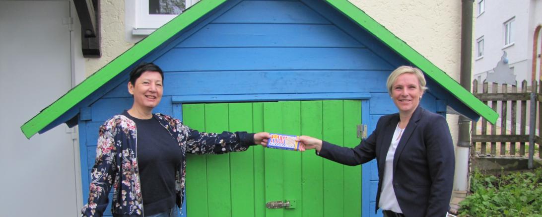 Das Bild zeigt die Familienbeauftragte des Landkreises Donau-Ries, Ursula Leinfelder (rechts) bei der Übergabe einer kleinen Aufmerksamkeit an Birgit Bayer, Leitung des Kindergarten St. Johannes in Rögling (links)