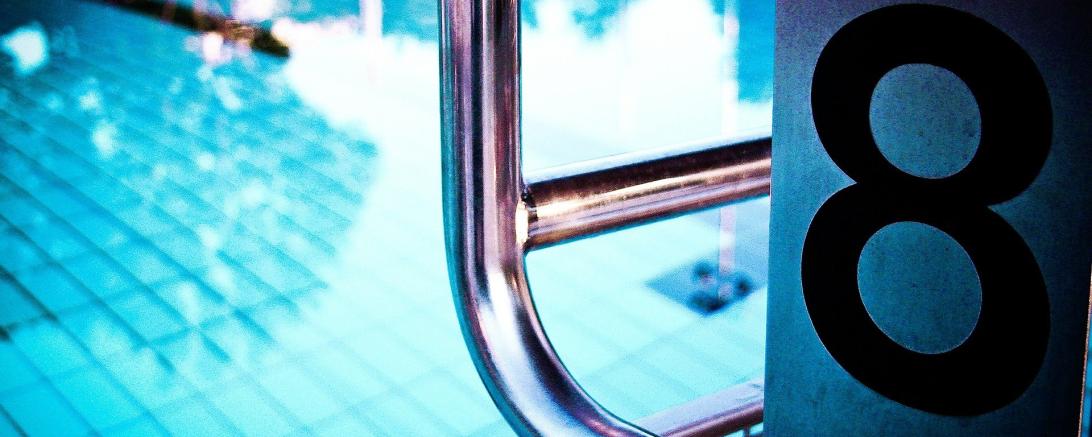 Es ist ein Teil eines Startblocks, sowie ein Ausschnitt aus einem Schwimmbecken zu sehen.