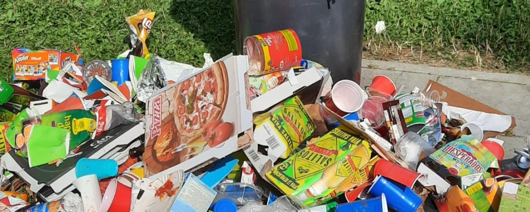 Das Bild zeigt einen überfüllten Mülleimer mit Müll um herum am Boden liegend. 