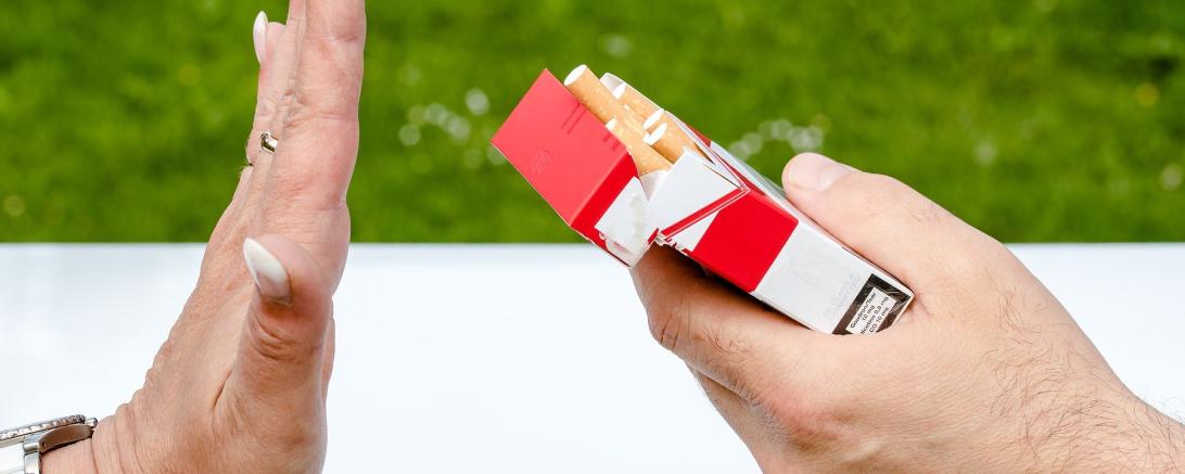 Zu sehen ist eine Hand die einer anderen eine Schachtel Zigaretten anbietet. Diese wird jedoch abgelehnt. 