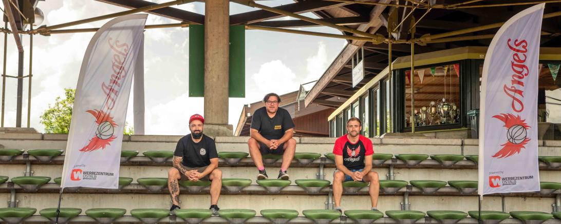 Drei Männer sitzen auf Stadiontribüne