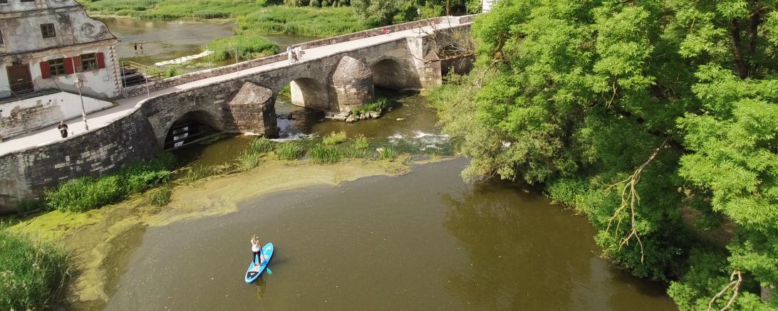 Wörnitz mit Steinerner Brücke, Stand-Up-Paddlerin auf dem Wasser, im Hintergrund die Harburg