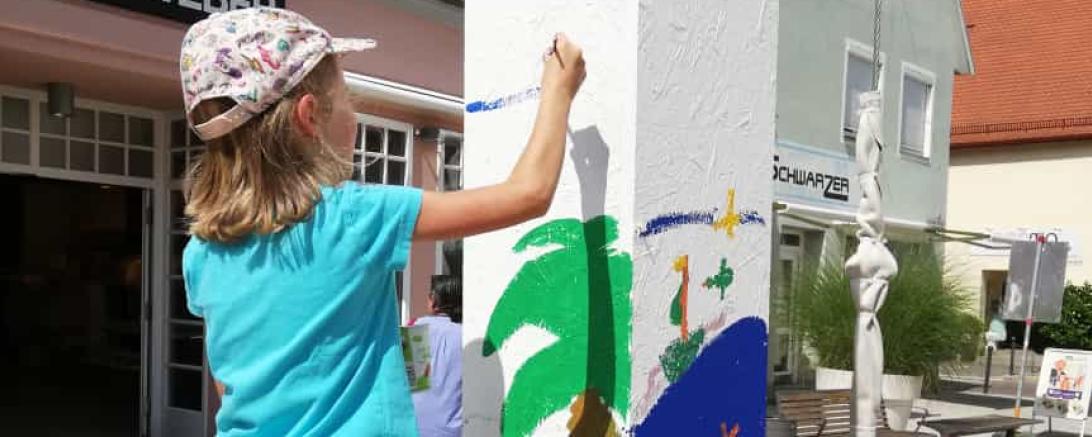 Kind steht auf kleiner Leiter und bemalt weiße Säule