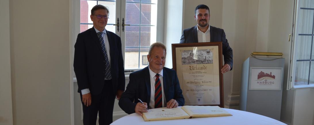 Altbürgermeister Wolfgang Kilian darf sich beim Festakt im Schloss Harburg auch in das goldene Buch der Stadt eintragen. Von links: Landrat Stefan Rößle, Altbürgermeister Wolfgang Kilian und der aktuelle Bürgermeister Christoph Schmidt. 