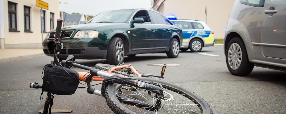das Bild zeigt einen Fahrradunfall mit einem Auto. 