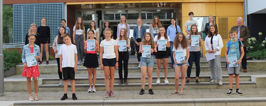 Kinder mit Urkunden und Schulleiter vor Schuleingang