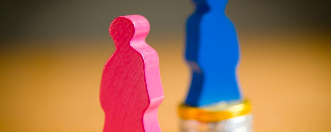 Pinke Holzfigur auf kleinem Münzstapel, blaue Figur auf größerem Münzstapel