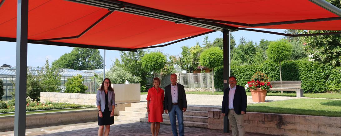 Vier Personen stehen unter einer großen, roten Doppelmarkise