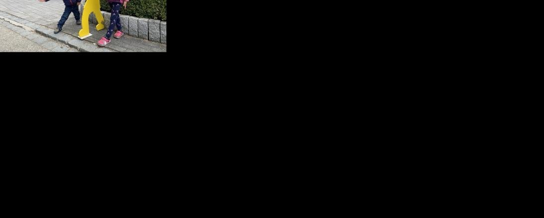 Gelbe Holzfigur auf Gehweg, daneben ein Junge und ein Mädchen, Gesichter unkenntlich gemacht