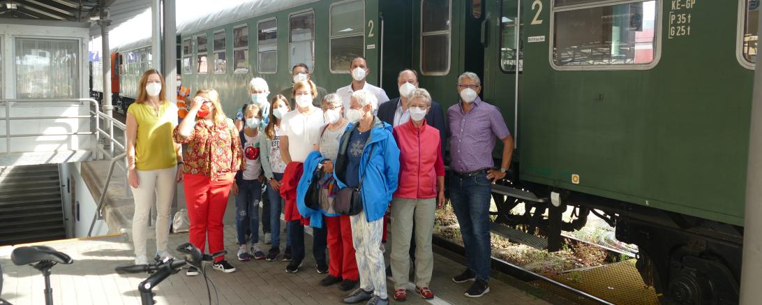 14 Personen mit FFP2-Masken stehen an Bahnhof vor Zugwaggon
