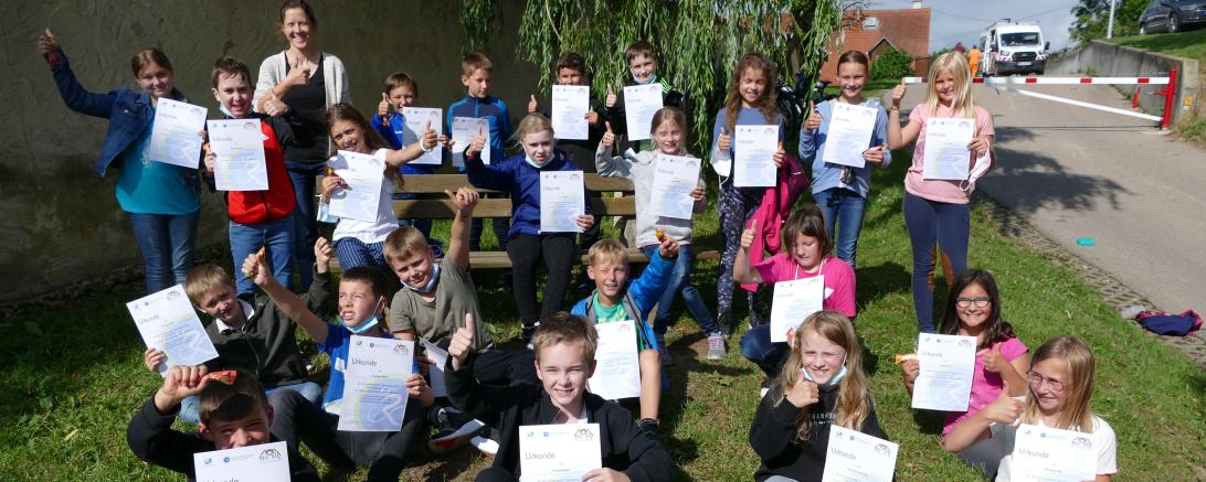 Auf dem Bild sind die Schüler*innen der dritten und vierten Klasse zu sehen. Neben einer Urkunde haben sie außerdem eine süße Belohnung erhalten. 