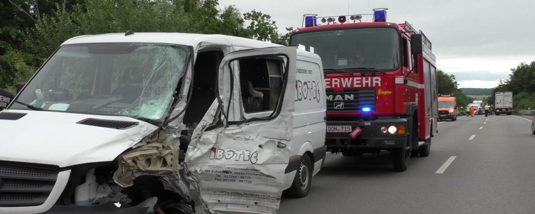 Beschädigter weißer Kleintransporter auf Straße, dahinter Feuerwehrauto