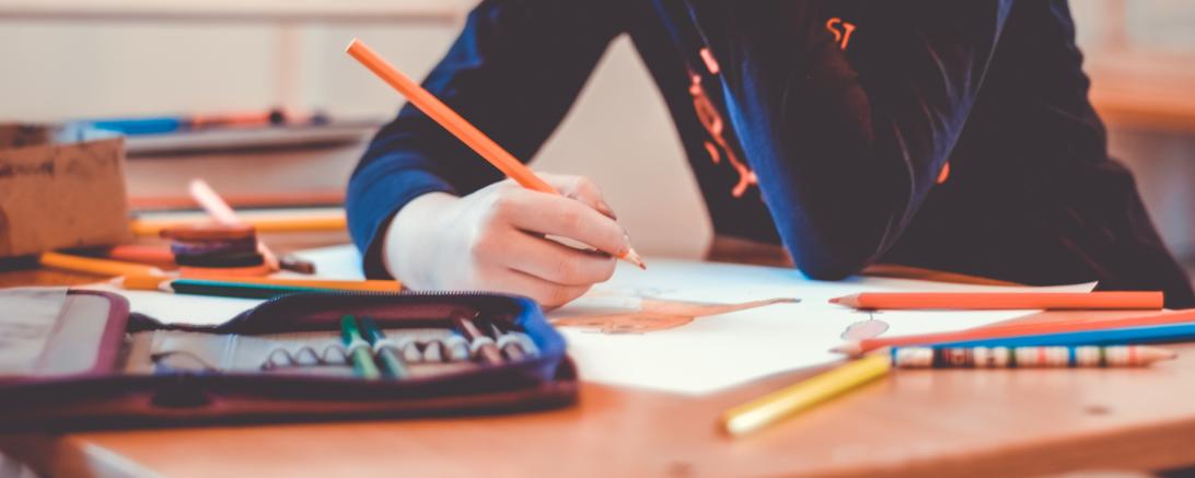 Schülerin sitzt an Schulbank mit Schreibutensilien