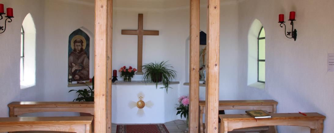 Innenraum einer Kapelle mit Betbänken und Altar mit Kreuz