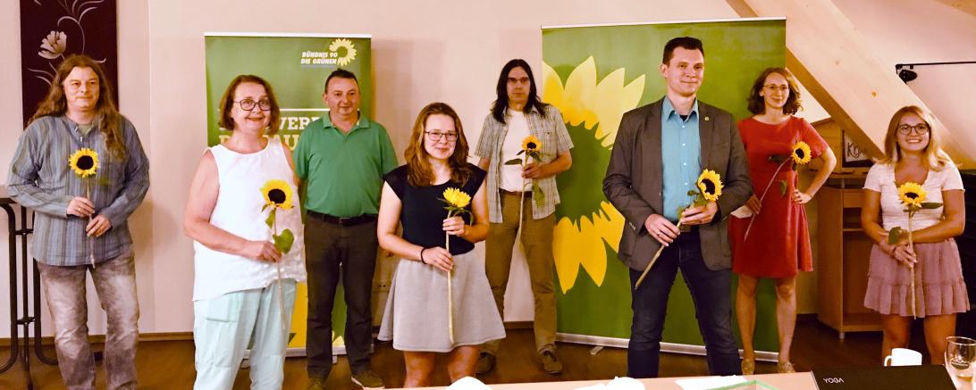Acht Personen mit Sonnenblumen vor Roll-Ups von Bündnis90/Die Grünen