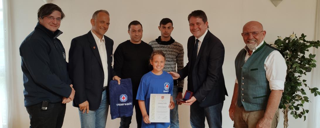 Das Bild zeigt: Johanna (in der Bildmitte mit Urkunde) mit (von links) Benjamin Schäfer (Technischer Leiter Kreiswasserwacht Nordschwaben), Michael Haller (Vorsitzender der Wasserwacht Ortsgruppe Asbach-Bäumenheim), die beiden Geretteten Ioan-Madalin Nistor und Ioan-Iosif Boca, Zweiter Bürgermeister Andreas Mayer und Erhard Schiele (Geschäftsführer ESG Kräuter GmbH).