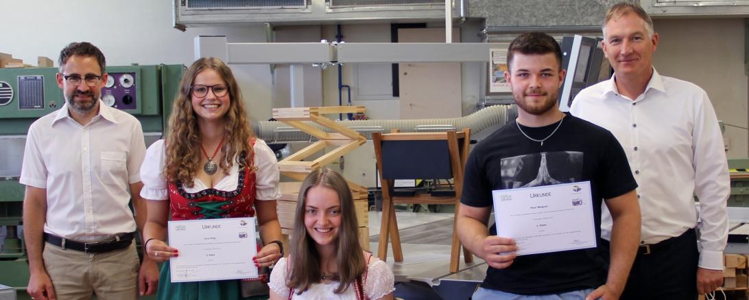 Zwei Schülerinnen in Tracht, ein Schüler und zwei Lehrkräfte in einer Werkstatt