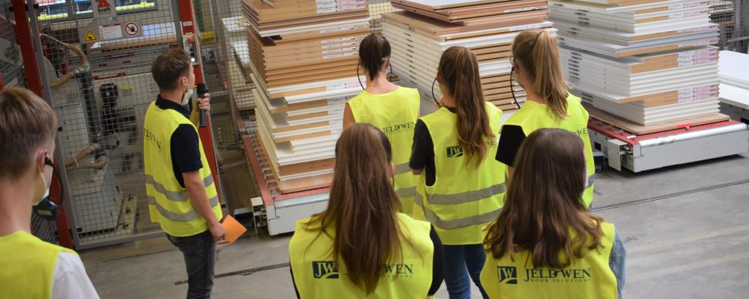 Sieben Personen in gelben Sicherheitswesten vor gestapelten Türen in Werkshalle