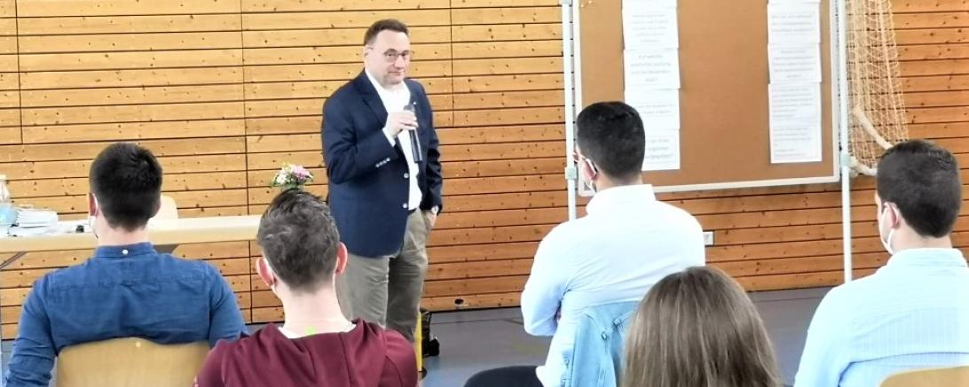 MdB Lange steht mit Mikrofon vor fünf Personen, die mit dem Rücken zum Bild sitzen