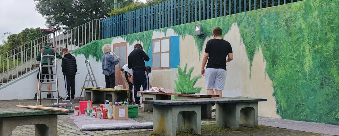 Aus Grau wurde Grün – aus der zuvor grauen Wand entstand unter oftmals grauen Himmel eine gemütlich anmutende Ecke im Pausenhof der Abt-Ulrich-Schule. Eine Ecke die zum Verweilen und staunen einlädt und anregt gemeinsam Großes zu schaffen.