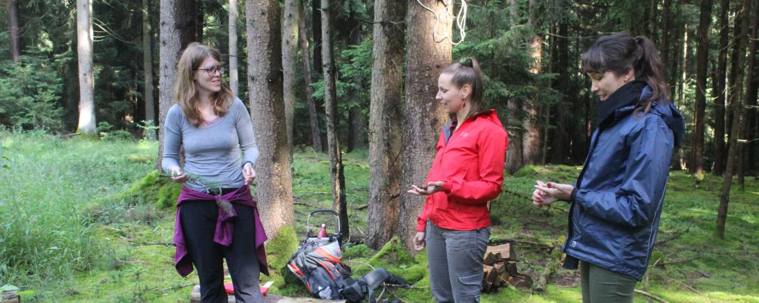 Auf dem Bild zu sehen drei Frauen bei Achtsamkeitsübungen im Wald.