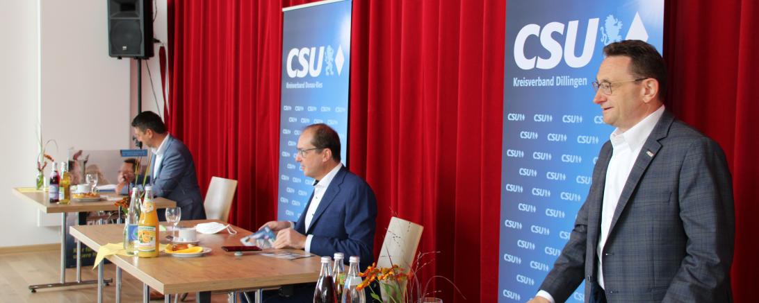 Drei Herren im Anzug an drei Tischen vor CSU-Roll-ups und rotem Vorhang