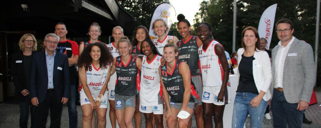 Basketballerinnen in Trikots mit Coach und Sponsoren