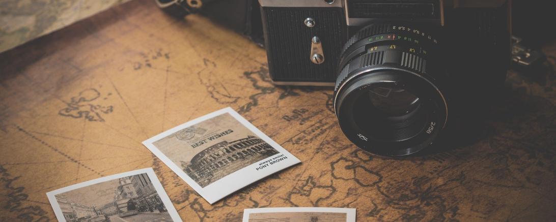 Auf dem Bild sieht man eine alte Kamera. Vor ihr liegen Polaroid Bilder von Reisen.