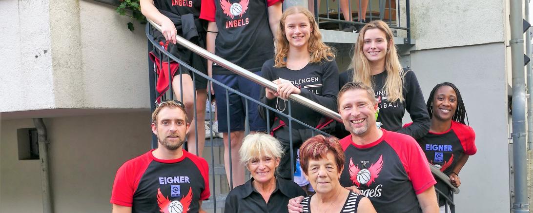 Basketballerinnen mit Funktionären und Wirtin auf Wendeltreppe