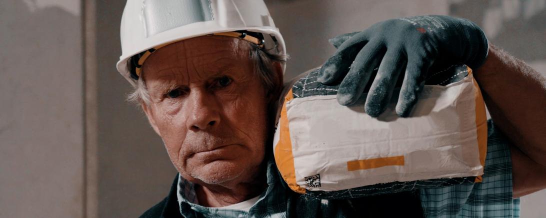 Bauarbeiter im Rentenalter schleppt Sack Zement auf der Schulter