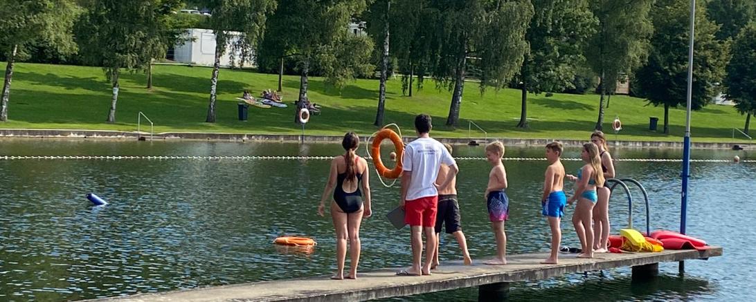 Auf dem Bild zu sehen die Kinder am Wasser mit Rettungsringen.