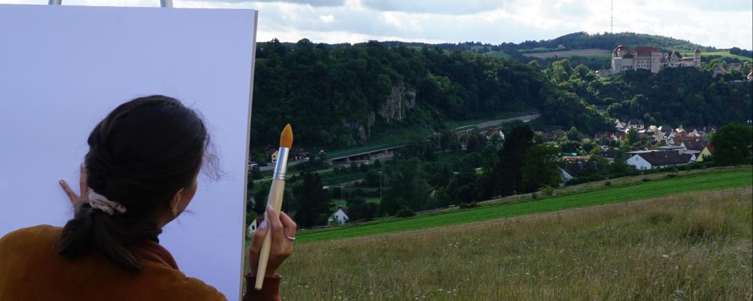 Auf dem Bild zu sehen eine Staffelei vor der Burg Harburg.