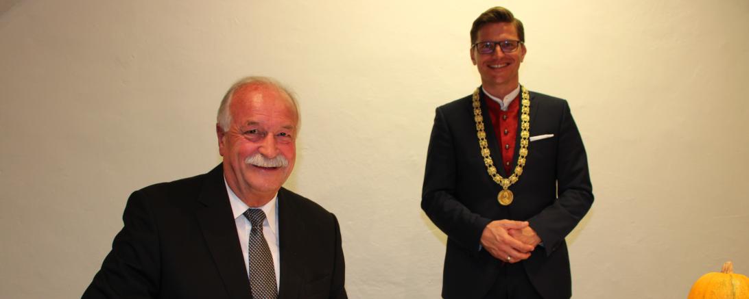 Hermann Faul sitzt an Tisch und trägt sich in Goldenes Buch der Stadt ein, dahinter steht OB David Wittner