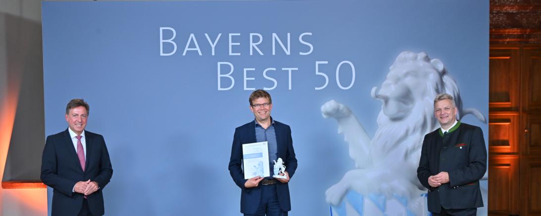 Das Foto zeigt (von links nach rechts) Prof. Dr. Thomas Edenhofer, Partner der Kanzlei Baker Tilly (Juror), Jürgen Schuster, Geschäftsführer der Raumschmiede GmbH, sowie Roland Weigert, Staatssekretär im Bayerischen Wirtschaftsministerium, bei der Preisverleihung.