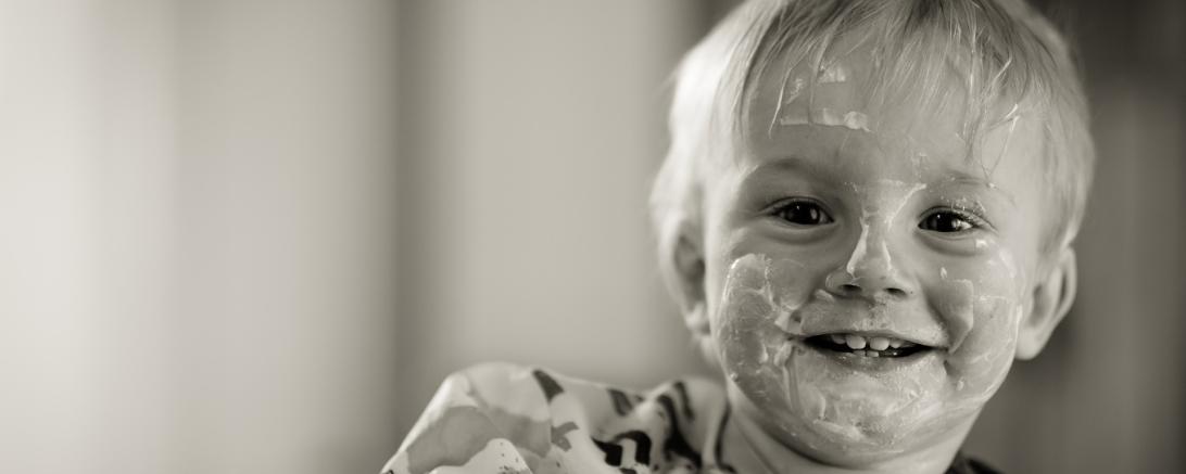 Auf dem Bild sieht man ein Kleinkind, das mit Jogurth verschmiert ist.