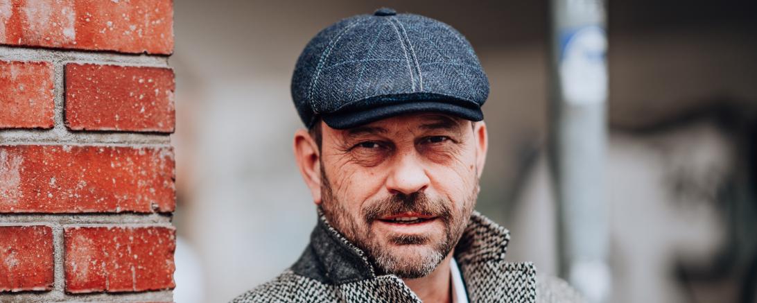 Michel Guillaume mit Mantel und Mütze an Backsteinmauer