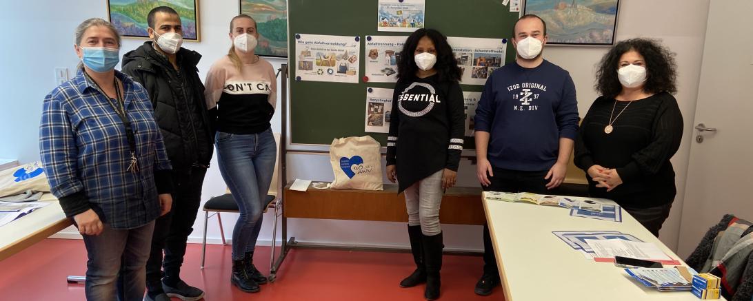 Zwei Männer und vier Frauen stehen vor Tafel in Klassenzimmer