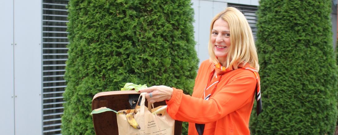 Auf dem Bild ist eine Frau abgebildet, die ihren Müll in der Biotonne entsorgt. 