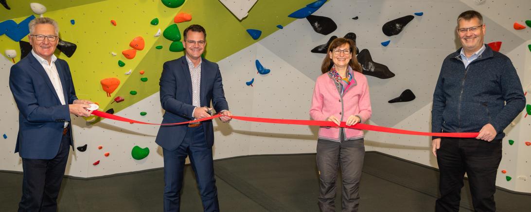 Vier Personen vor Boulderwand halten rotes Band