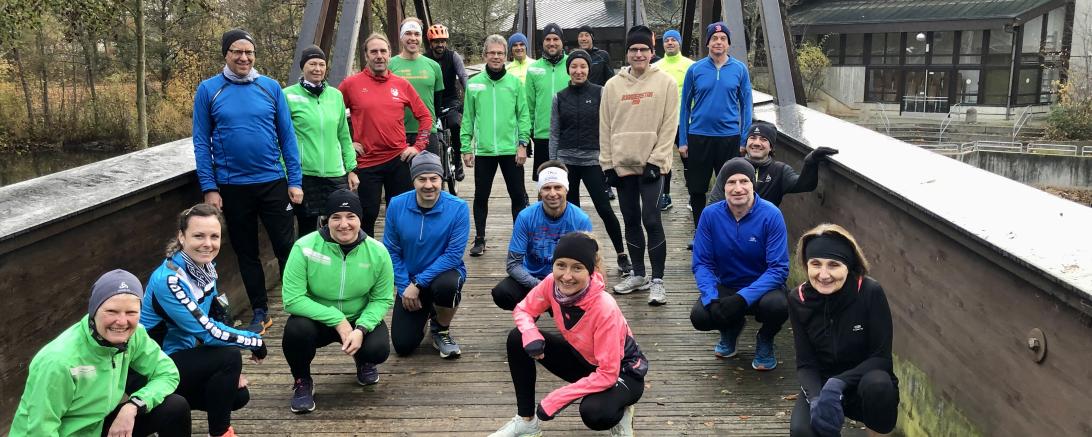 Personen in winterlicher Sportkleidung stehen oder knien auf Brücke in Vorbereitung auf den Jedermannslauf