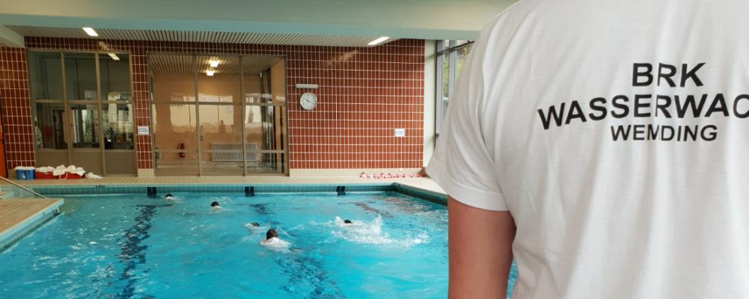 Mann mit T-Shirt-Aufdruck BRK Wasserwacht Wemding steht an Rand eines Beckens im Hallenbad