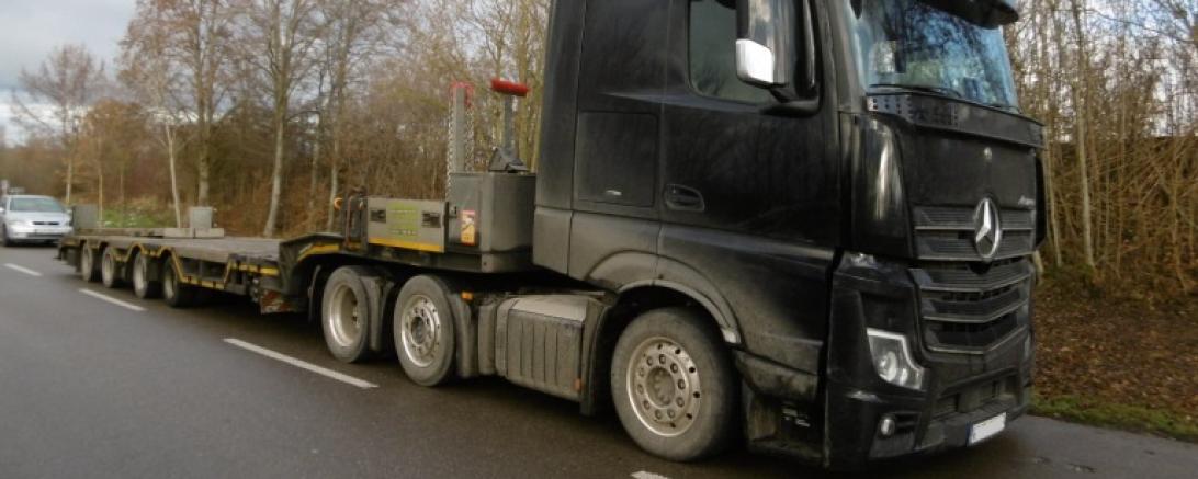 Schwarzer Sattelzug mit Tiefbettschwertransportauflieger steht am Straßenrand