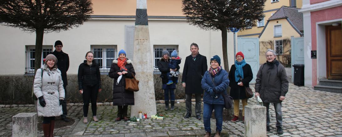 Das Bild zeigt die Teilnehmenden der Gedenkveranstaltung, darunter: vorne links Stadträtin Andrea Eireiner, zweite links von der Stele Kreisvorsitzende Elisa Pfaff, links neben der Stele die 1. Vorsitzende des Freundeskreis Synagoge Hainsfahrt e.V. Sigi Atzmon, rechts von der Stele der Bezirksrat der Grünen und Donauwörther Stadtrat Albert Riedelsheimer.