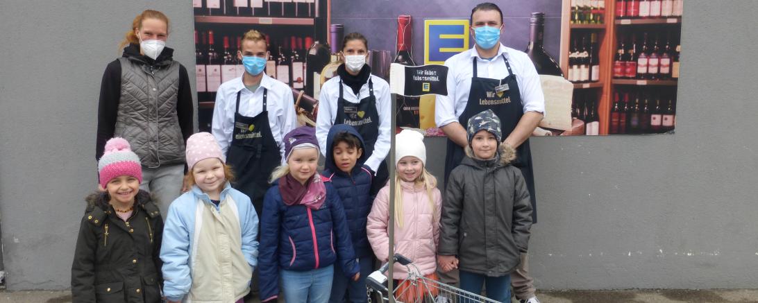 Zu sehen sind Mitarbeiter des Edeka-Marktes und die Kinder der Tagesstätte bei der Übergabe des Einkaufswagens. 