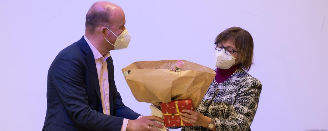 Blumen und ein verpacktes Geschenk werden an Dr. Ruth Kilian übergeben.