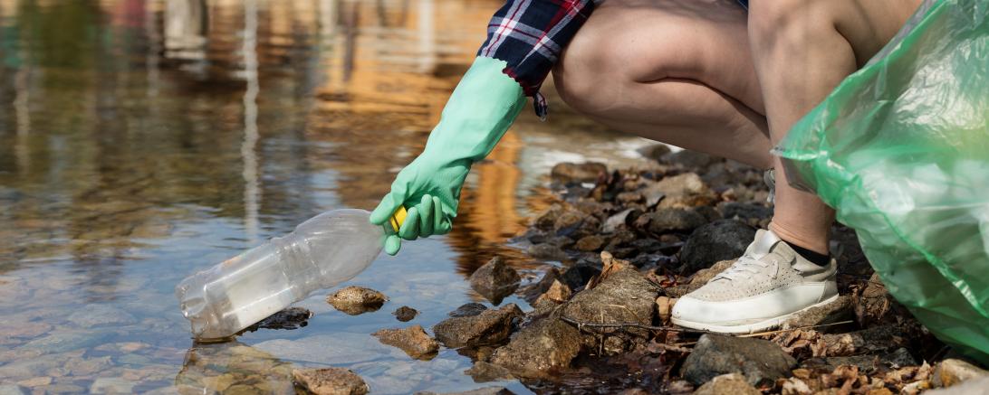 Frau sammelt Plastikflasche aus Gewässer